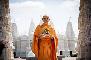 Mahant Swami Maharaj holding a decorated deity idol at BAPS Shri Swaminarayan Mandir HD wallpaper