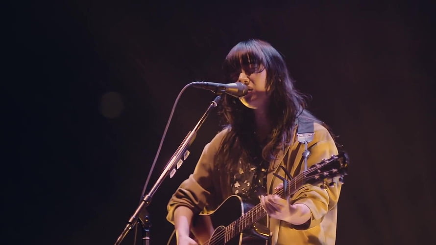 Aimyon performing live on stage with acoustic guitar and microphone under warm spotlight HD wallpaper
