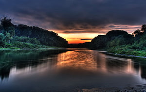 Dramatic River Sunset with Dark Clouds and Golden Reflections in a Forested Valley HD wallpaper