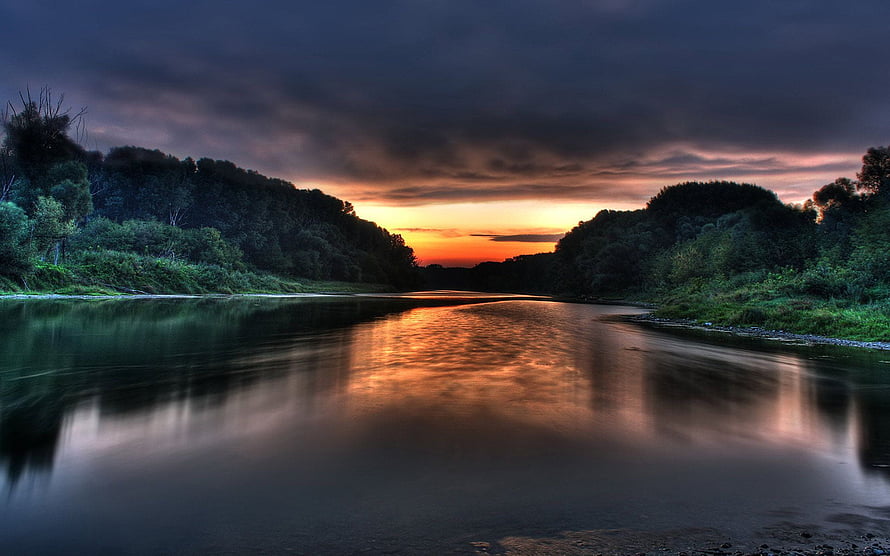 Dramatic River Sunset with Dark Clouds and Golden Reflections in a Forested Valley HD wallpaper