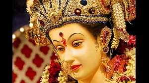 Close-up of a beautifully adorned Hindu goddess idol wearing a jeweled crown and floral garlands HD wallpaper