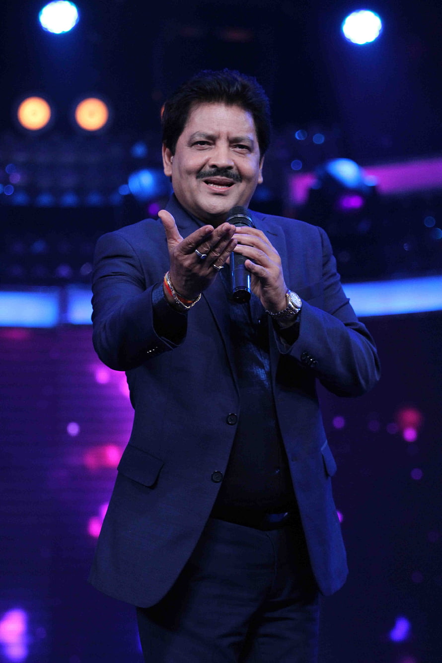 Udit Narayan performing on stage in a dark suit with microphone under blue and purple concert lighting HD phone wallpaper