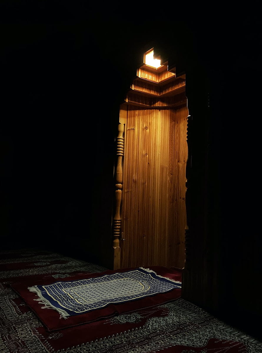 Illuminated Wooden Mihrab with Prayer Rug in a Dark Mosque Interior HD phone wallpaper