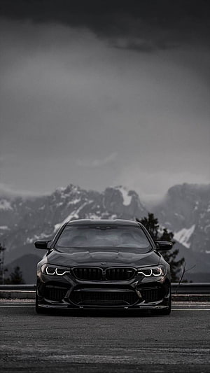 Black BMW M5 F90 Front View on Mountain Road with Snowy Peaks and Dramatic Sky HD phone wallpaper