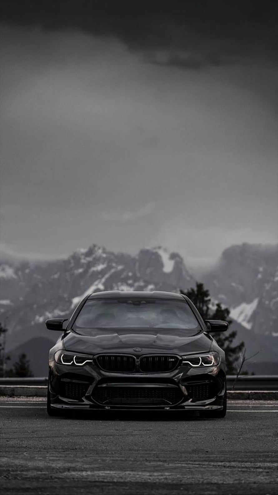 Black BMW M5 F90 Front View on Mountain Road with Snowy Peaks and Dramatic Sky HD phone wallpaper