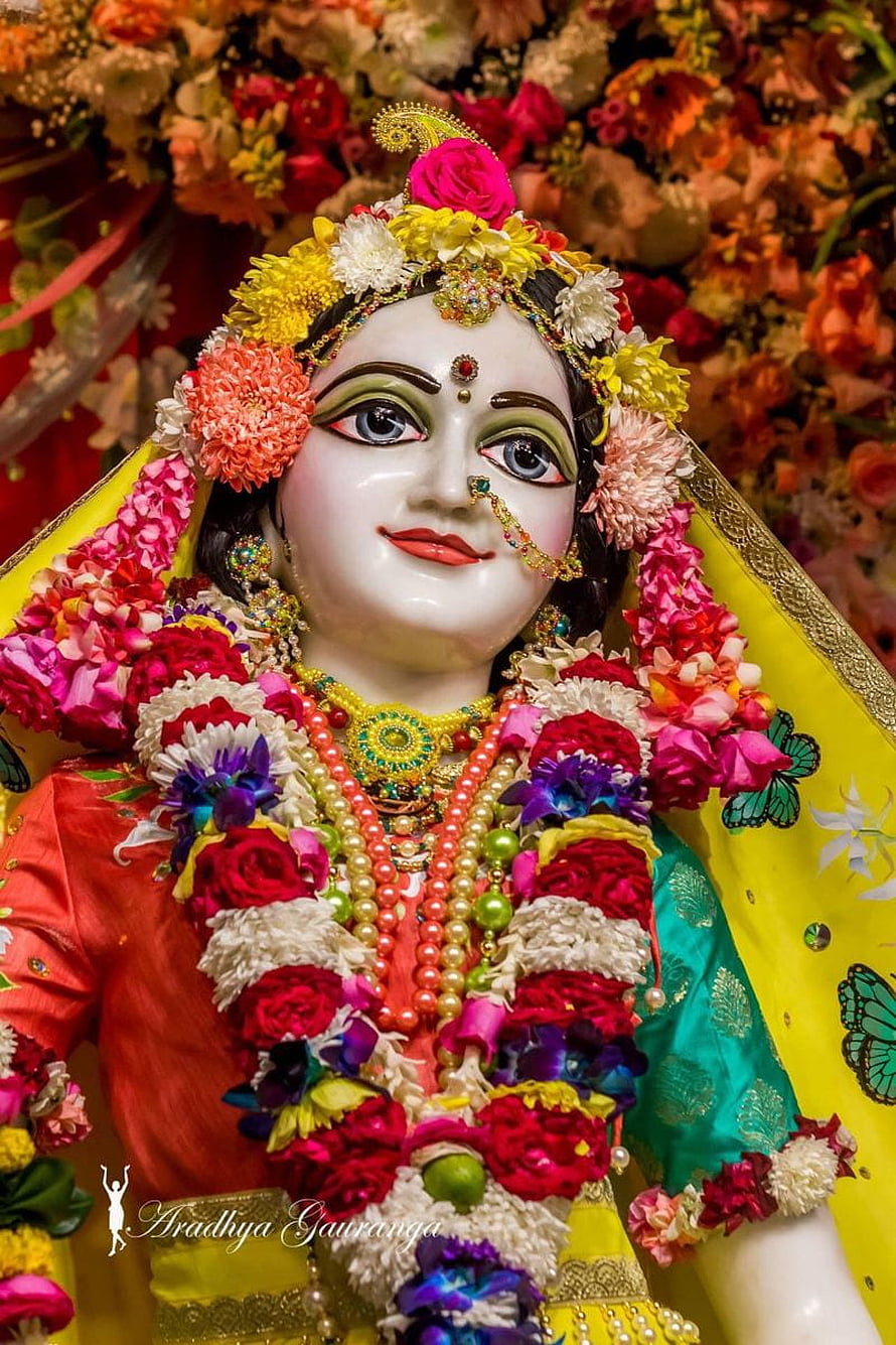 Beautifully adorned Radha statue with vibrant floral garlands and traditional jewelry HD phone wallpaper