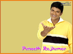 Puneeth Rajkumar smiling in a yellow sweater with a black stripe against a beige background HD wallpaper