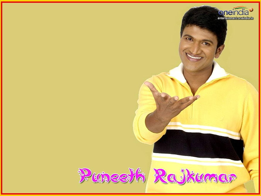 Puneeth Rajkumar smiling in a yellow sweater with a black stripe against a beige background HD wallpaper