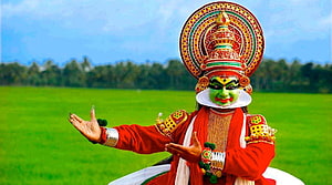Kathakali dancer in traditional green makeup and elaborate headdress performing in a lush green field HD wallpaper