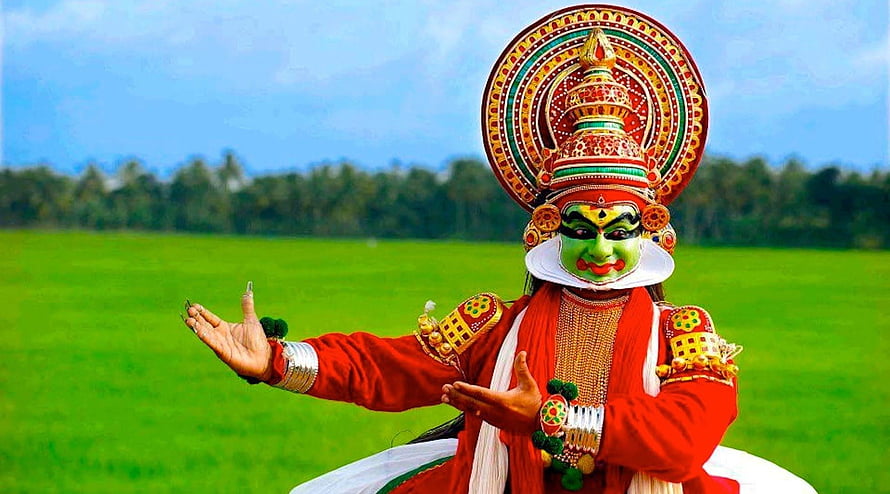 Kathakali dancer in traditional green makeup and elaborate headdress performing in a lush green field HD wallpaper
