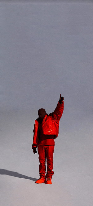 Kanye West in a vibrant red outfit pointing upward against a minimalist grey backdrop HD phone wallpaper