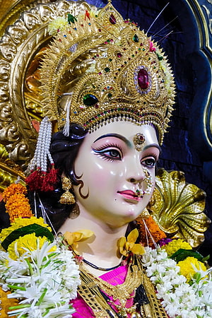 Close-up of a beautifully adorned Hindu goddess statue wearing a golden crown and floral garlands HD phone wallpaper