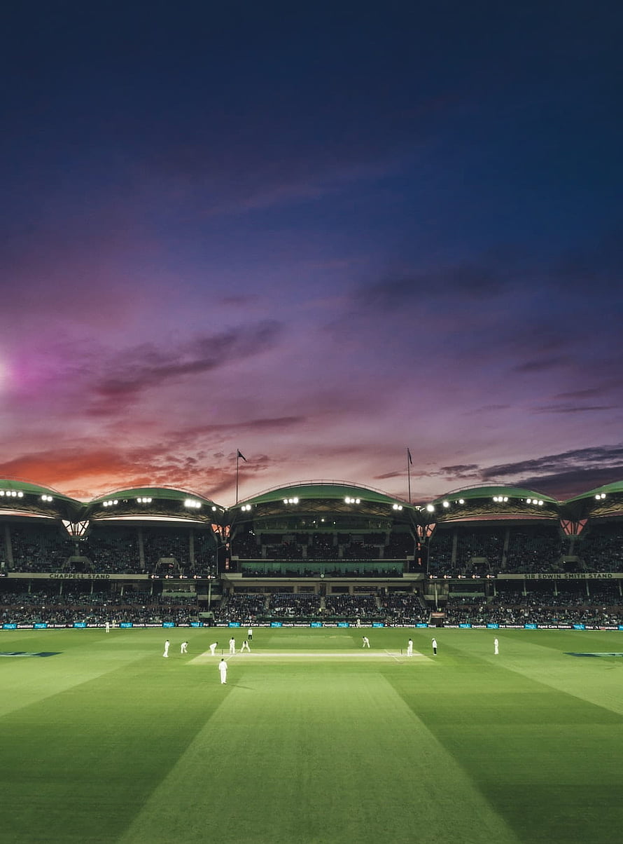 Lords Cricket Ground at dusk with players on the field under a vibrant purple and orange sky HD phone wallpaper