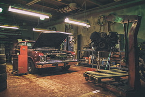 Vintage Muscle Car Under Repair in a Cluttered Auto Shop with Engine Hoist HD wallpaper