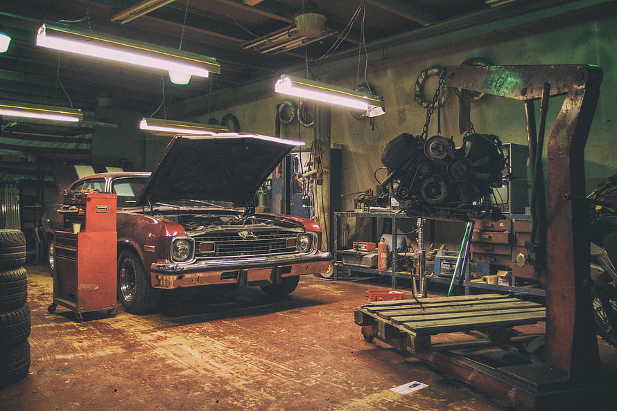 Vintage Muscle Car Under Repair in a Cluttered Auto Shop with Engine Hoist HD wallpaper