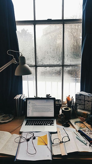 Cozy study desk setup with laptop and books by a rainy window HD phone wallpaper
