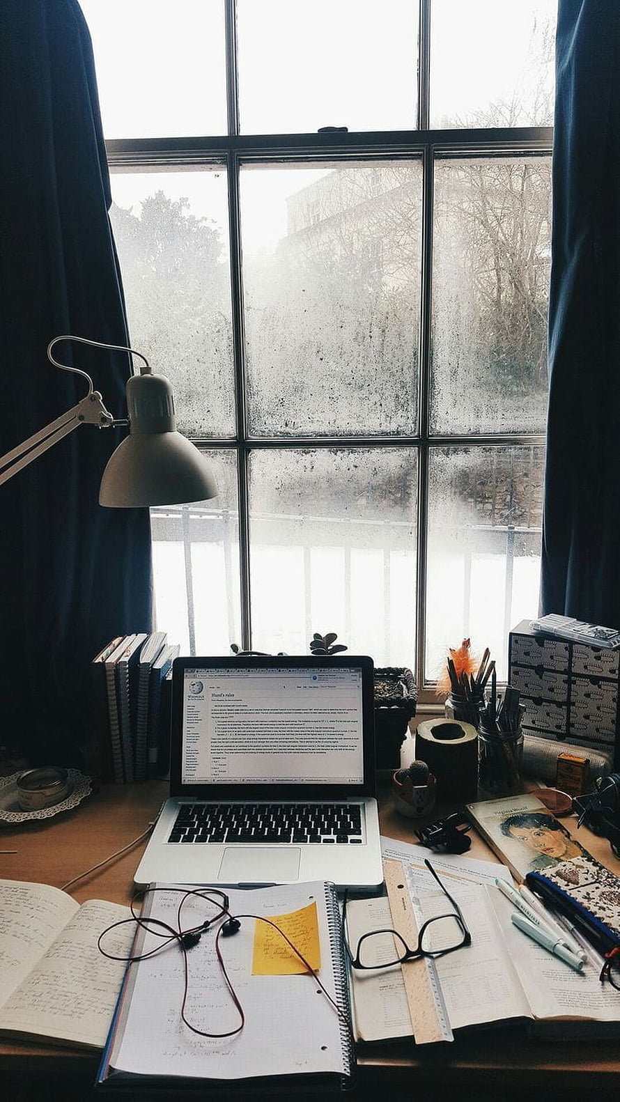 Cozy study desk setup with laptop and books by a rainy window HD phone wallpaper