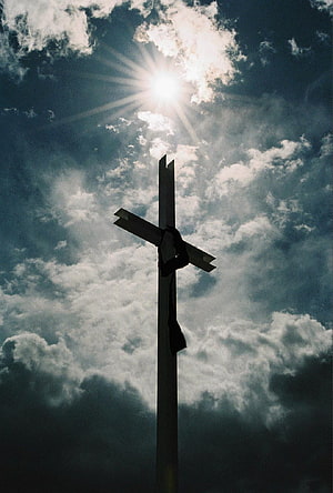 Silhouette of a wooden cross against a dramatic cloudy sky with sunburst rays HD phone wallpaper