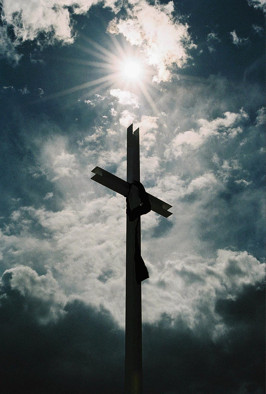 Silhouette of a wooden cross against a dramatic cloudy sky with sunburst rays HD phone wallpaper