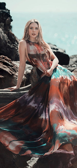 Elizabeth Olsen in a flowing patterned gown on a rocky coastal cliff HD phone wallpaper