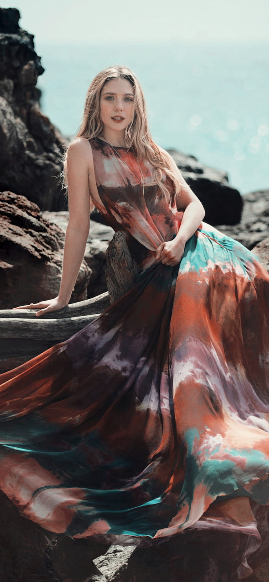 Elizabeth Olsen in a flowing patterned gown on a rocky coastal cliff HD phone wallpaper