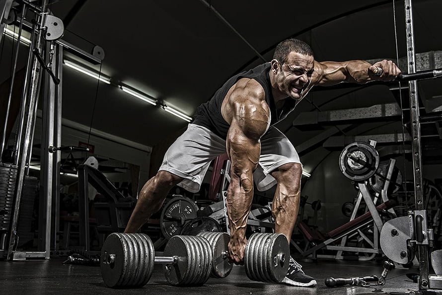 Muscular Athlete Performing Intense Dumbbell Row in Dark Gym Setting HD wallpaper