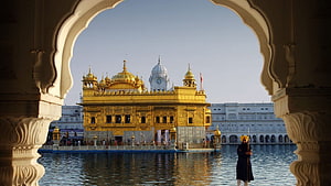 Golden Temple Amritsar framed by ornate archway with guard and sacred pool HD wallpaper