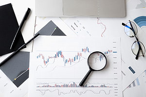 Financial Analysis Workspace With Candlestick Charts, Magnifying Glass, and Trading Documents HD wallpaper