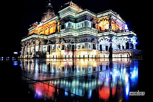 Prem Mandir Vrindavan illuminated at night with colorful reflections on wet pavement HD wallpaper