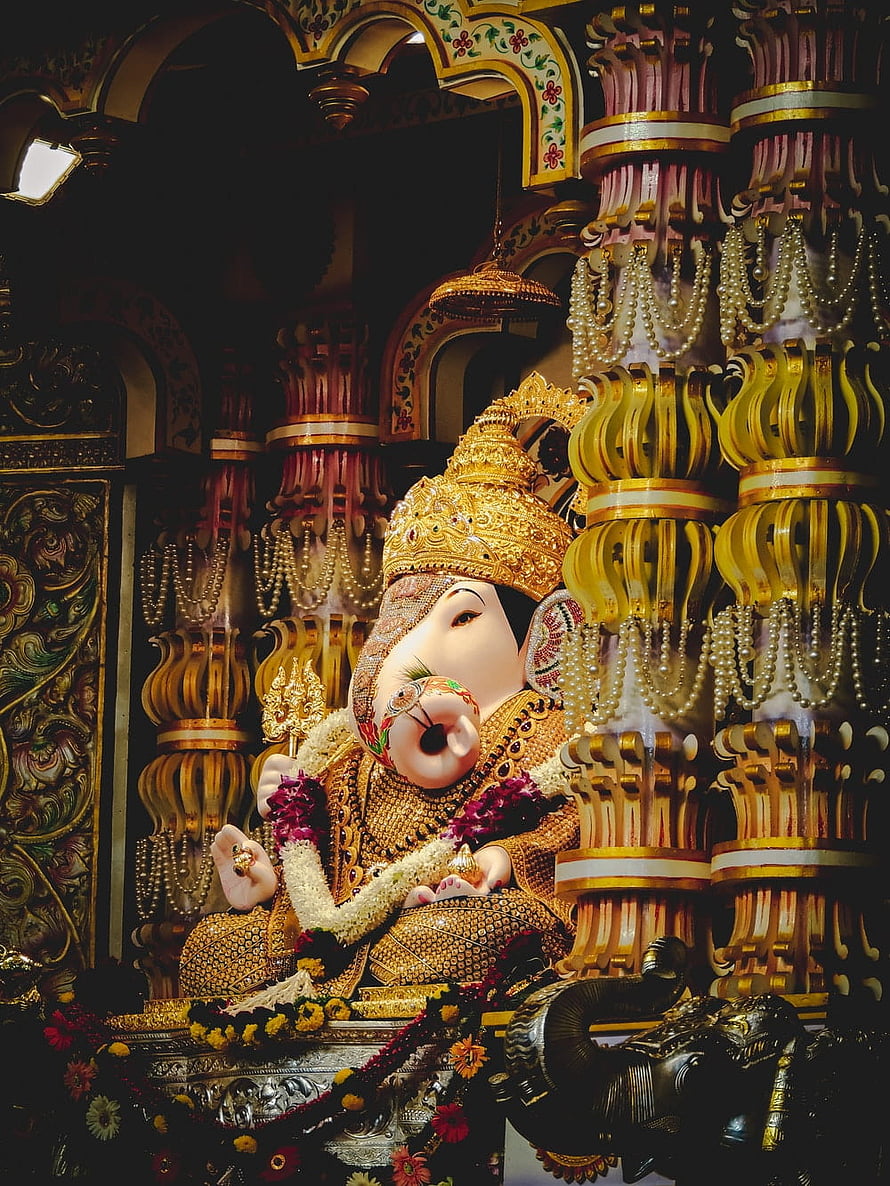Ornate Golden Ganesha Statue in Temple with Intricate Pillars and Floral Offerings HD phone wallpaper