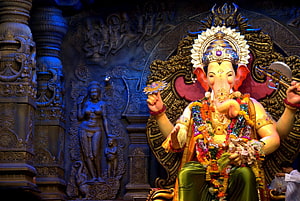 Vibrant Ganesha Statue in Temple with Intricate Carvings and Floral Garlands HD wallpaper