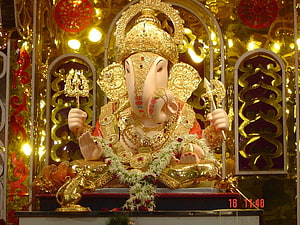 Golden Ganesha Idol With Floral Garland And Temple Decor HD wallpaper