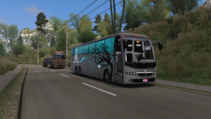 Grey coach bus with blue tree livery driving on a scenic mountain road in a realistic simulation game HD wallpaper