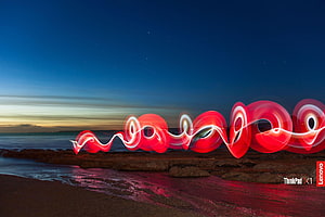 Red Light Painting Spirals on Rocky Beach at Night HD wallpaper
