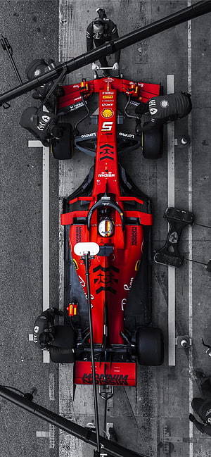 Top-down view of a red Ferrari Formula 1 race car in the pit lane with mechanics working on it HD phone wallpaper