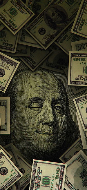 Close-up of Benjamin Franklin's face on a hundred dollar bill surrounded by scattered US currency HD phone wallpaper