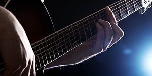 Close-up of a hand pressing guitar strings on a dark fretboard with dramatic blue backlighting HD wallpaper