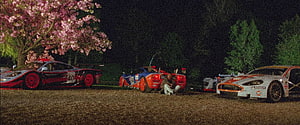 Nighttime scene with three racing cars parked on gravel beneath a blooming cherry blossom tree HD wallpaper