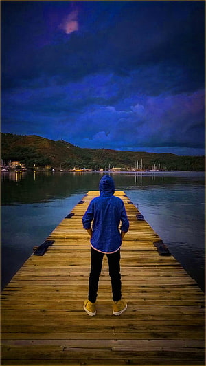 Person in Blue Hoodie Standing on Wooden Pier at Dusk HD phone wallpaper