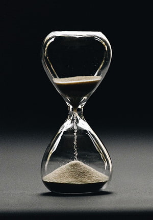 Classic Glass Hourglass With Flowing Sand Against a Dark Background HD phone wallpaper