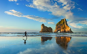 Runner Silhouette on Wet Sand at Wharariki Beach with Pancake Rocks and Blue Sky HD wallpaper