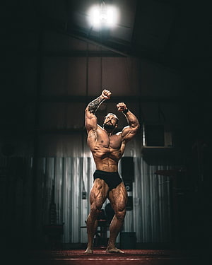 Muscular Bodybuilder Posing Under Spotlight in Dark Gym HD phone wallpaper