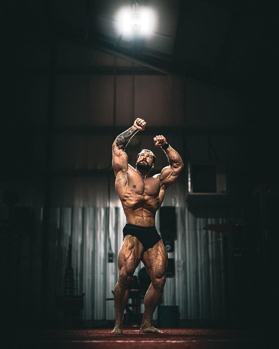 Muscular Bodybuilder Posing Under Spotlight in Dark Gym HD phone wallpaper