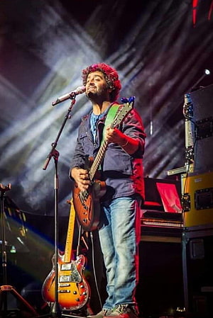 Arijit Singh performing live on stage with electric guitar and microphone under concert lighting HD phone wallpaper