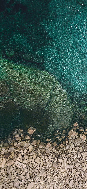Aerial View of Turquoise Water Overlapping a Rocky Shoreline with Clear Ripples HD phone wallpaper