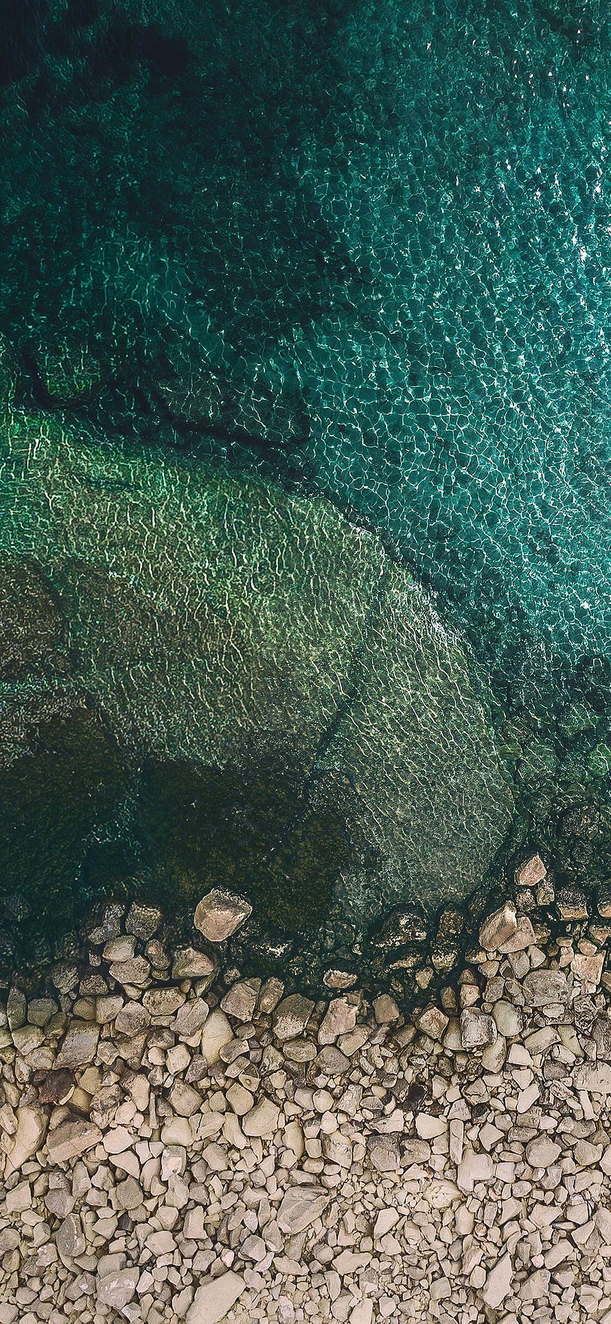 Aerial View of Turquoise Water Overlapping a Rocky Shoreline with Clear Ripples HD phone wallpaper