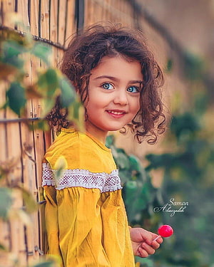 Smiling Girl with Curly Hair in Yellow Dress Holding a Lollipop HD phone wallpaper