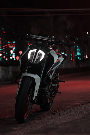 White KTM Duke motorcycle with glowing headlights parked on a street at night with colorful bokeh lights HD phone wallpaper