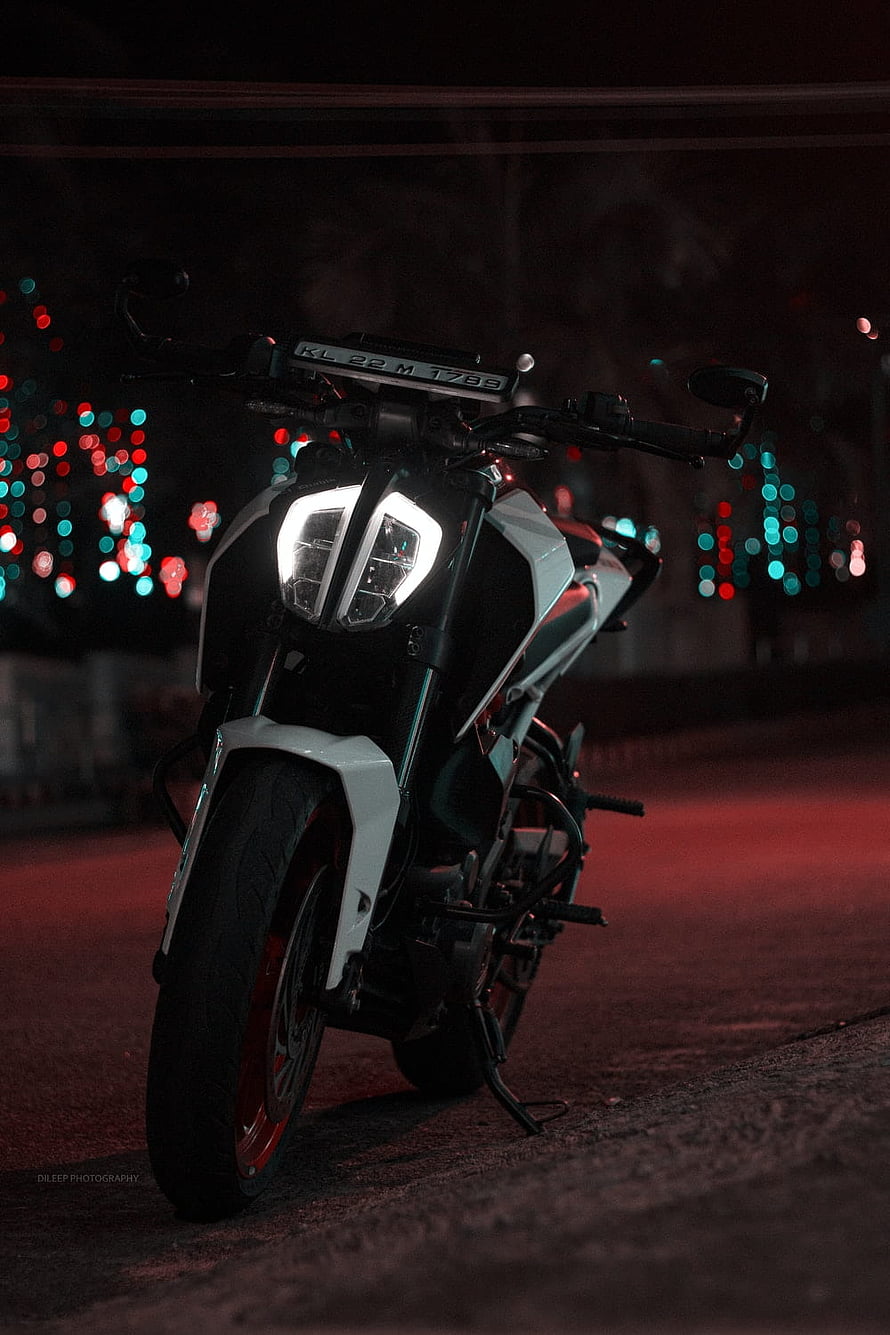 White KTM Duke motorcycle with glowing headlights parked on a street at night with colorful bokeh lights HD phone wallpaper