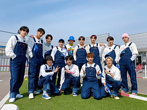 SEVENTEEN members posing in matching denim overalls on a sunny outdoor field HD wallpaper